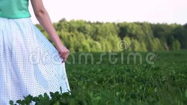 穿着<strong>白色连衣裙</strong>的女人或少女走在绿色的田野上，用手拿着<strong>连衣裙</strong>。